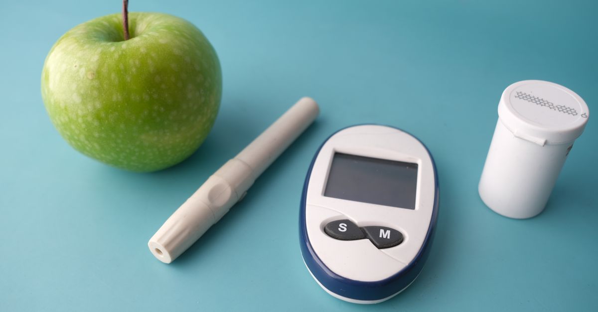 Flat lay of a glucose monitor, apple, and insulin pen on a pastel background.