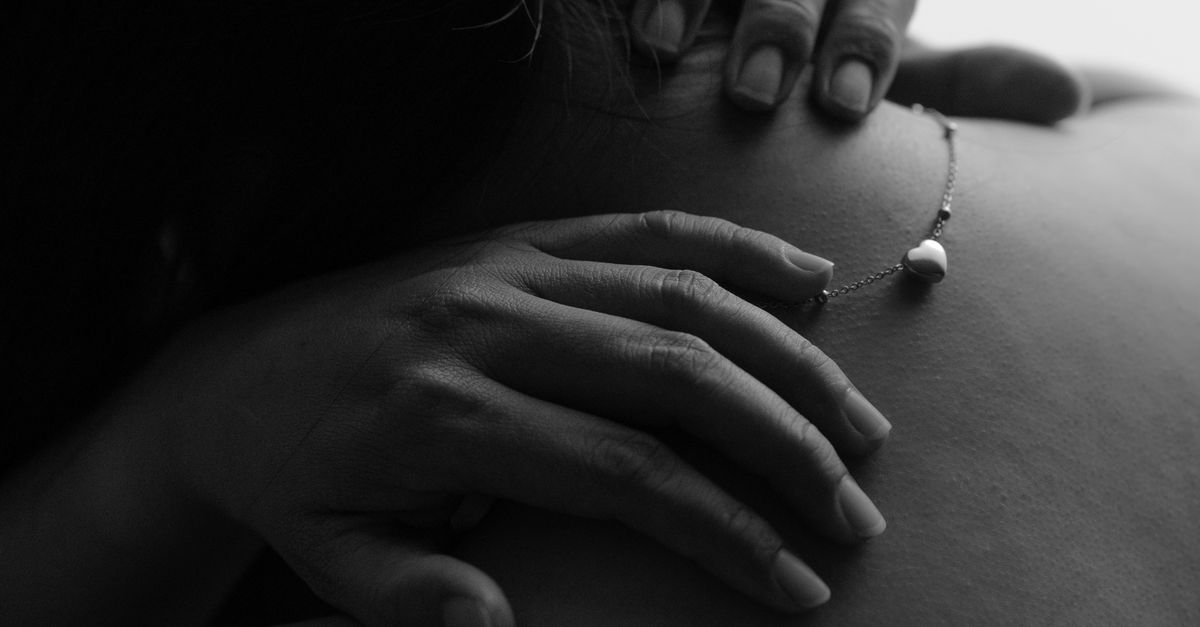 Black and white photo of hands gently resting on bare shoulders, conveying intimacy and tenderness.