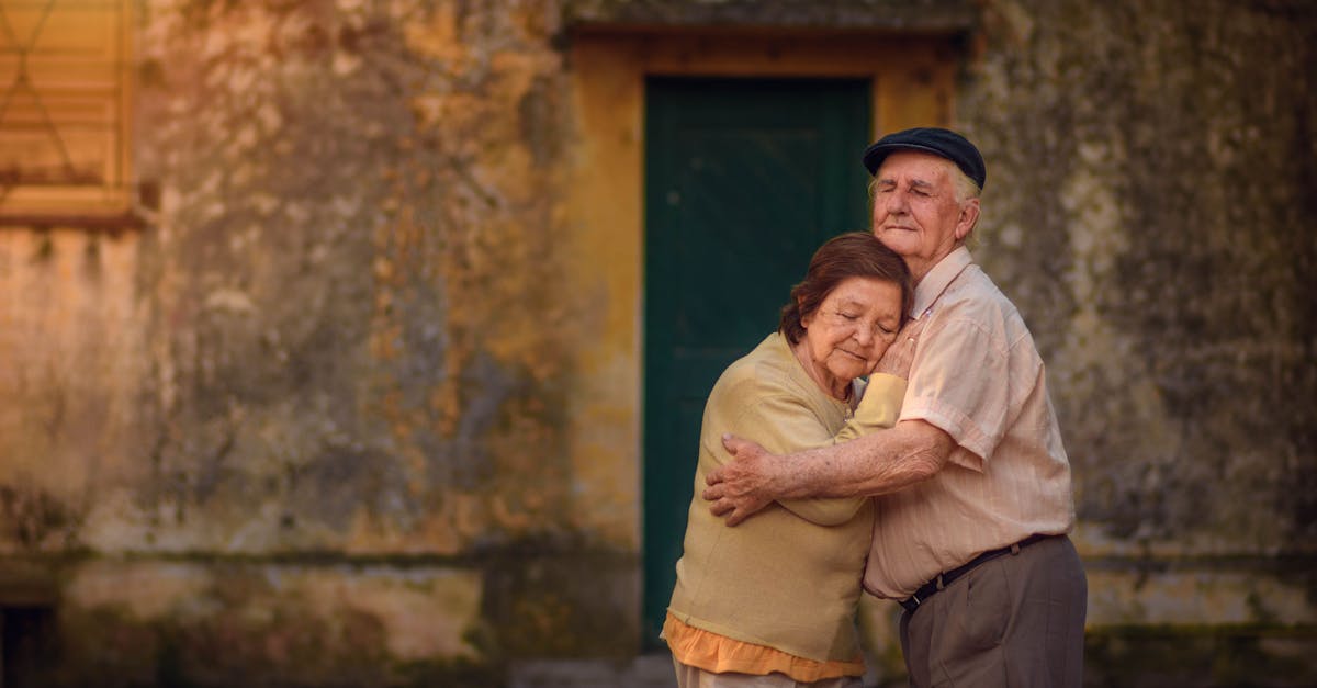 Charming elderly couple embracing warmly in front of a rustic building wall.