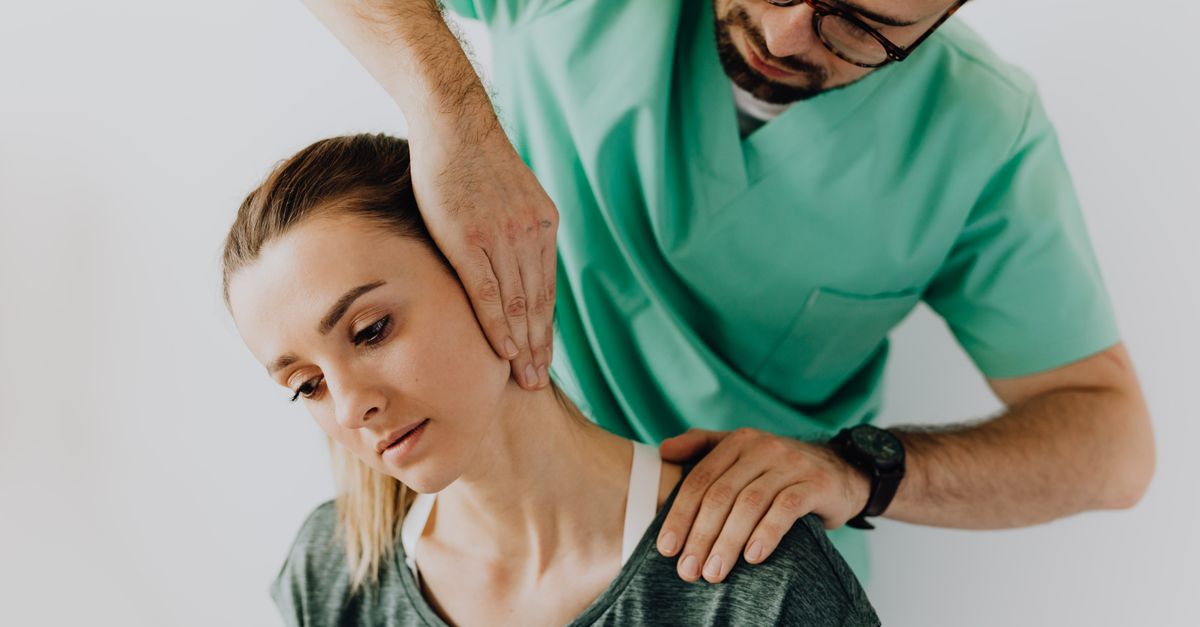 Confident doctor wearing uniform and eyeglasses gently doing therapeutic massage on calm female patients neck and stretching stiff neck muscles