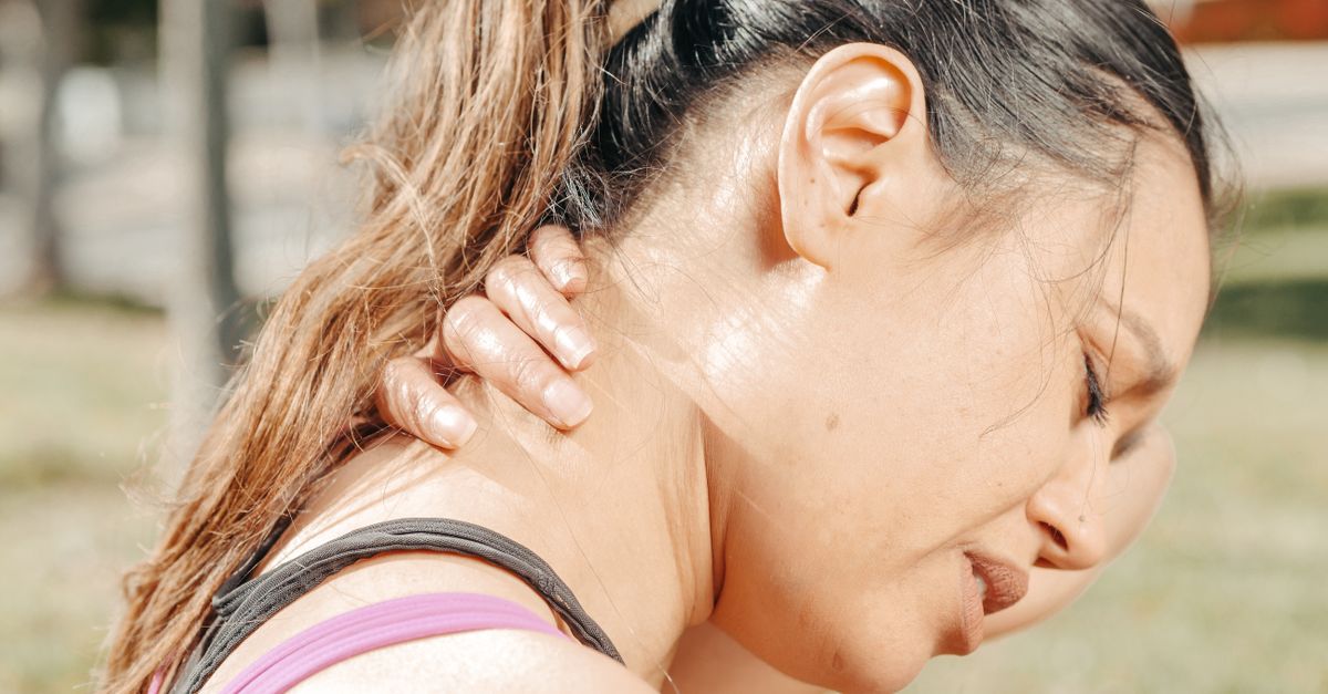 Close-up of a woman holding her neck, showing discomfort and pain outdoors.