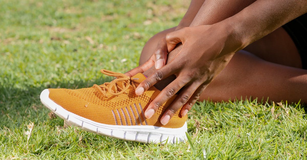 Person holding ankle in orange sneaker, suggesting potential sports injury.