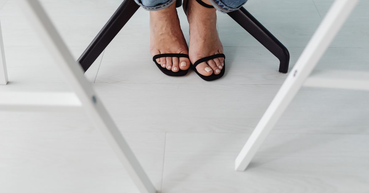 A person's feet and footwear resting under a table indoors.