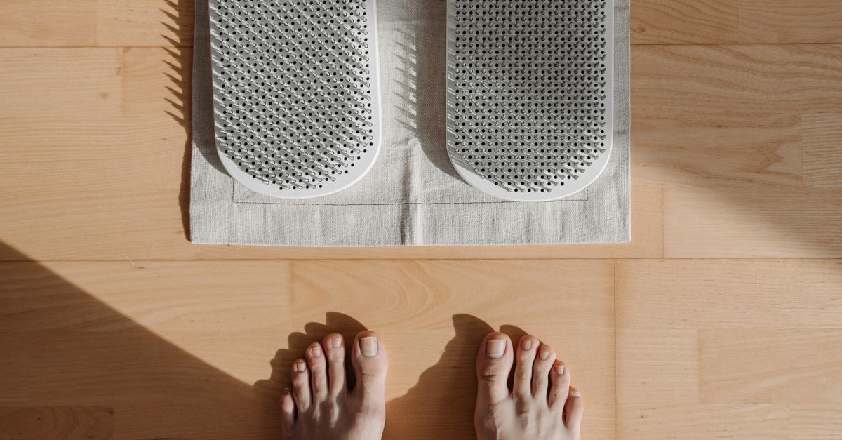 Close-up of bare feet on a wooden floor with acupressure mat, highlighting relaxation therapy.