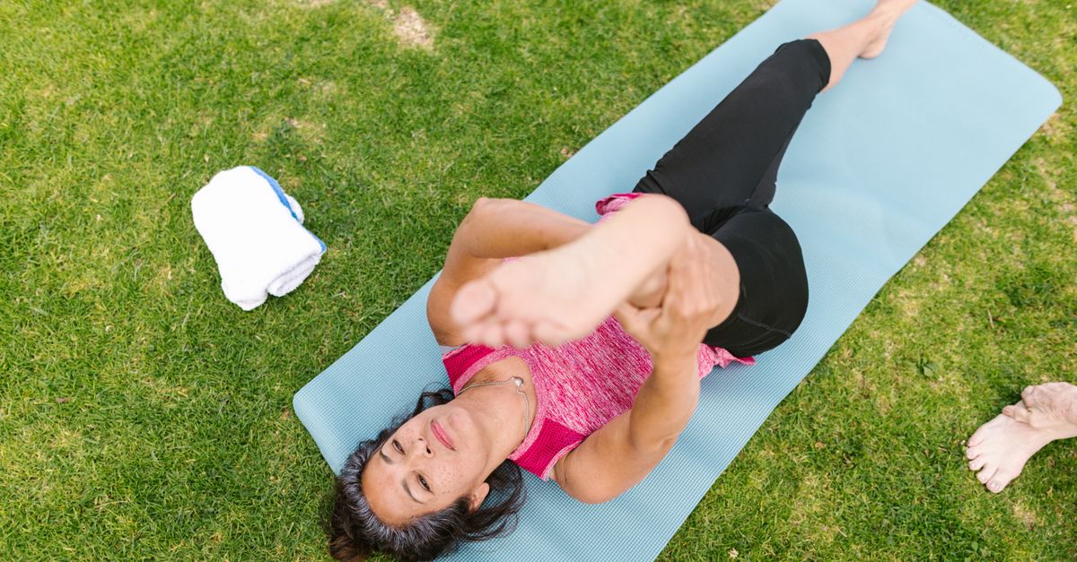Senior woman stretching on a yoga mat in a park, embracing outdoor wellness and fitness.