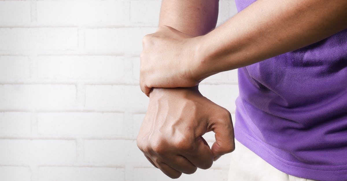 Close-up of a person holding their wrist in pain against a brick wall background.