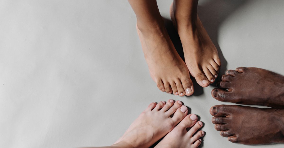 Close-up of three diverse pairs of barefooted feet standing on a white surface.