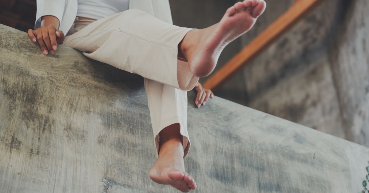 A woman sits barefoot indoors, relaxing her feet and hands.