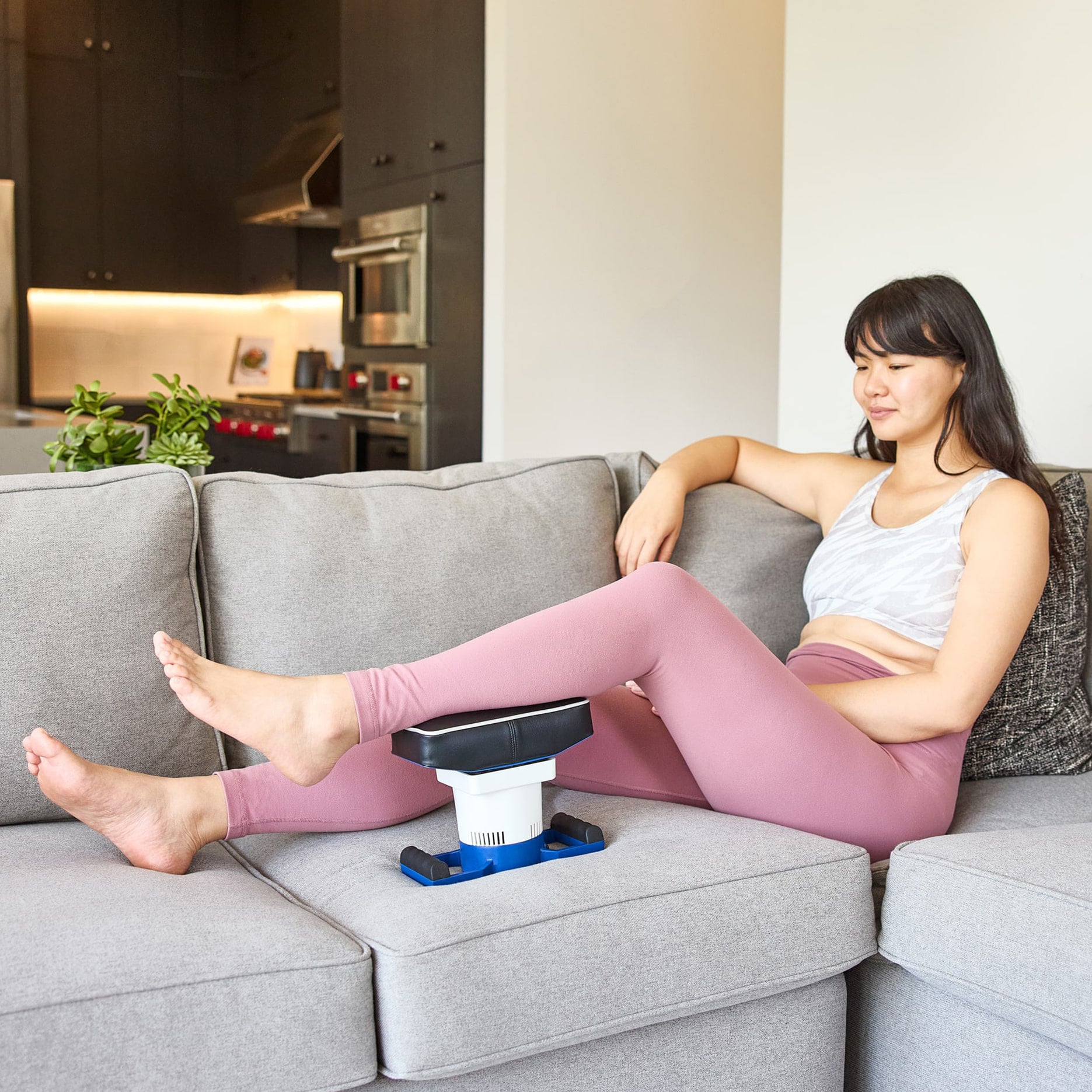 Woman lounging on a couch using a body massager classic on her calf