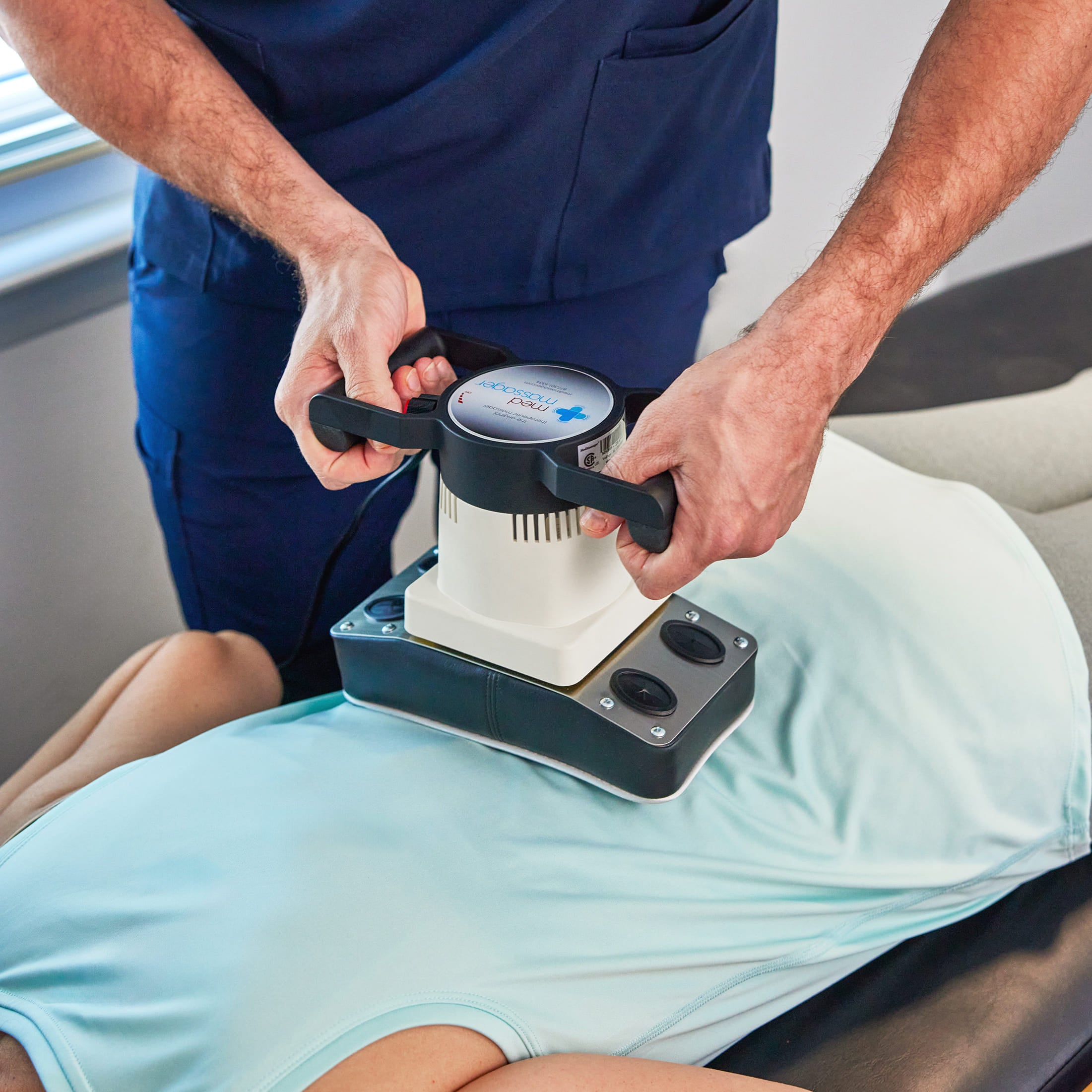 Practitioner using MedMassager body massager on a patient’s back in a clinical setting.