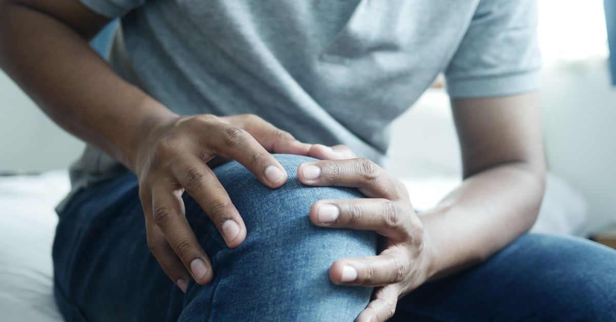 Close-up of a man holding his lower leg, a moment of discomfort in a casual indoor setting.
