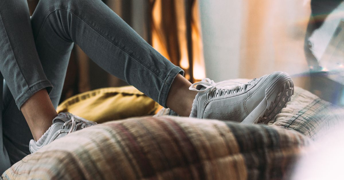Close-up of a person relaxing indoors with shoes and jeans resting on pillows.