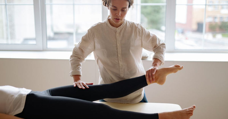 A therapist provides leg massage therapy to a client in a serene clinic setting.