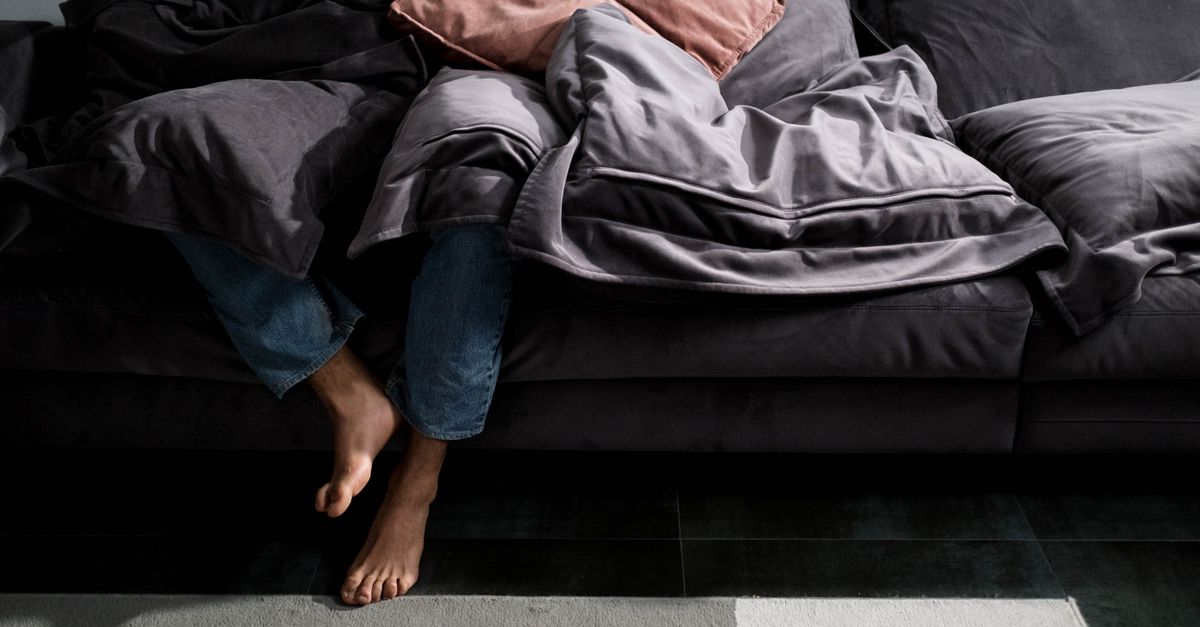 Person lounging on a sofa covered in blankets, showcasing a cozy and relaxed indoor setting.