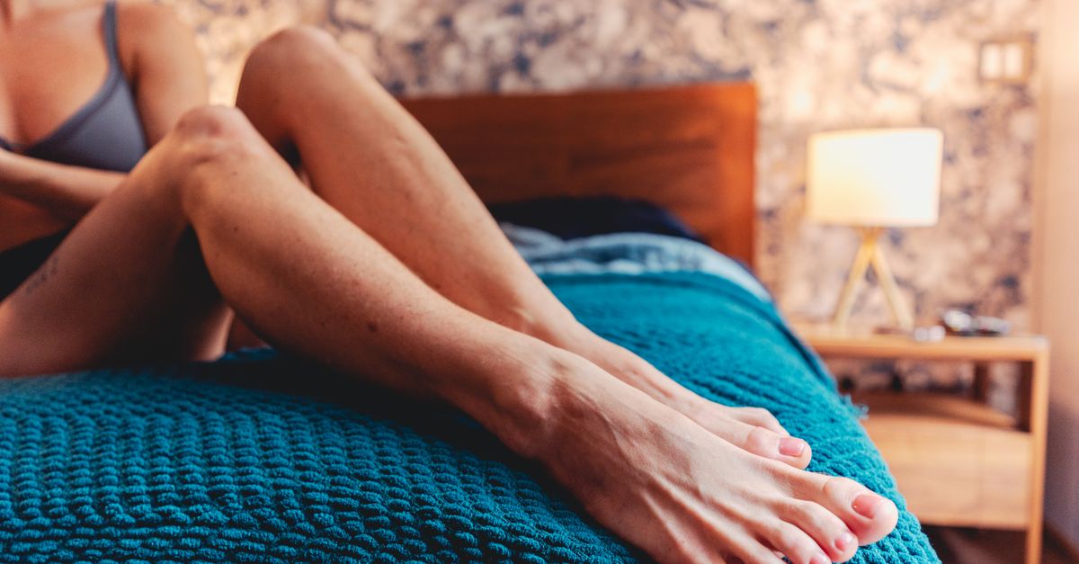 A woman relaxing on a bed with a cozy blue blanket in a warmly lit bedroom.