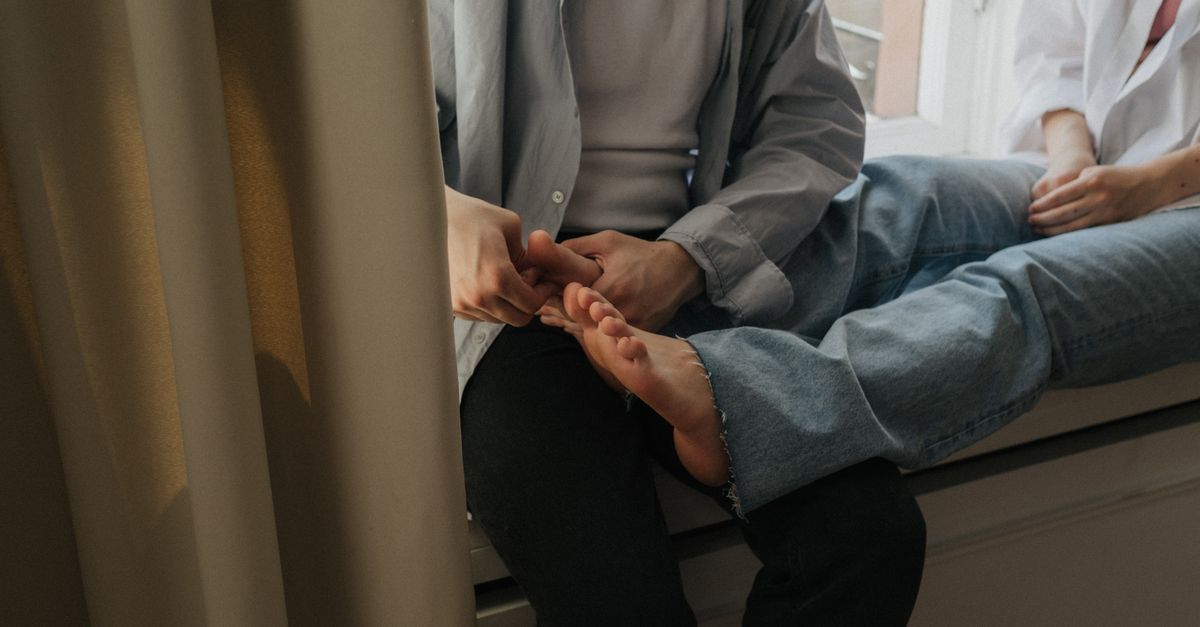 A couple enjoys a relaxing foot massage while sitting by the window indoors.