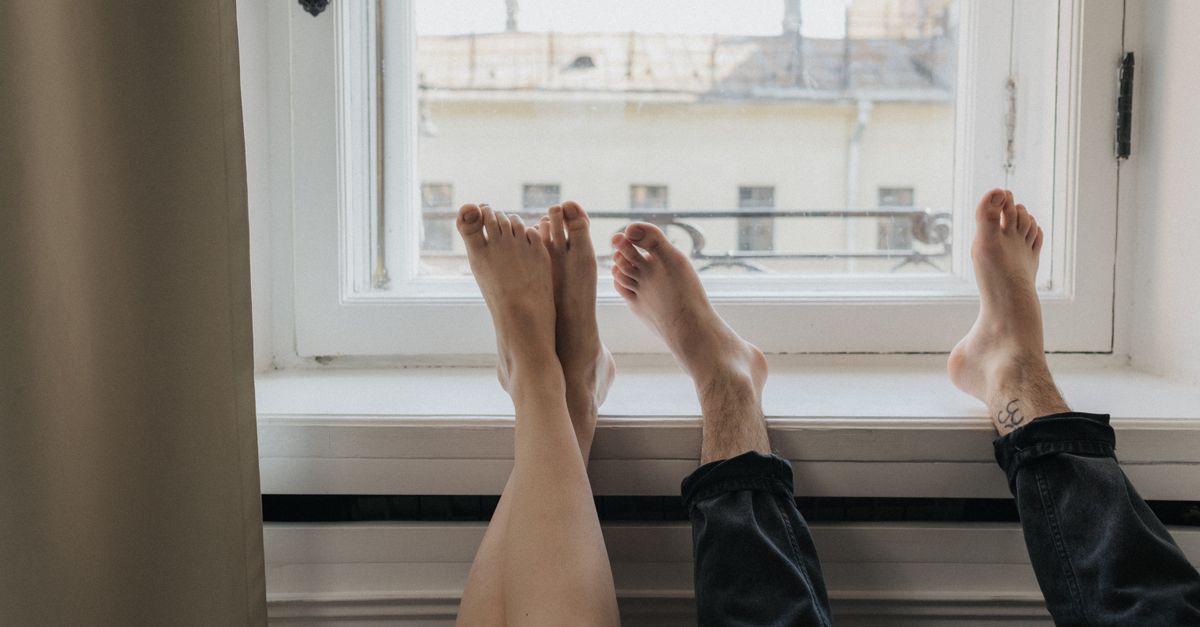 Two people resting barefoot by a sunlit window indoors.